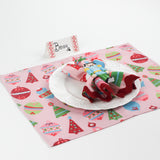 Side angle view of Harbor Trail Paper Place Card in pink and red on a Christmas-themed table with nutcracker napkin and festive pink placemat.