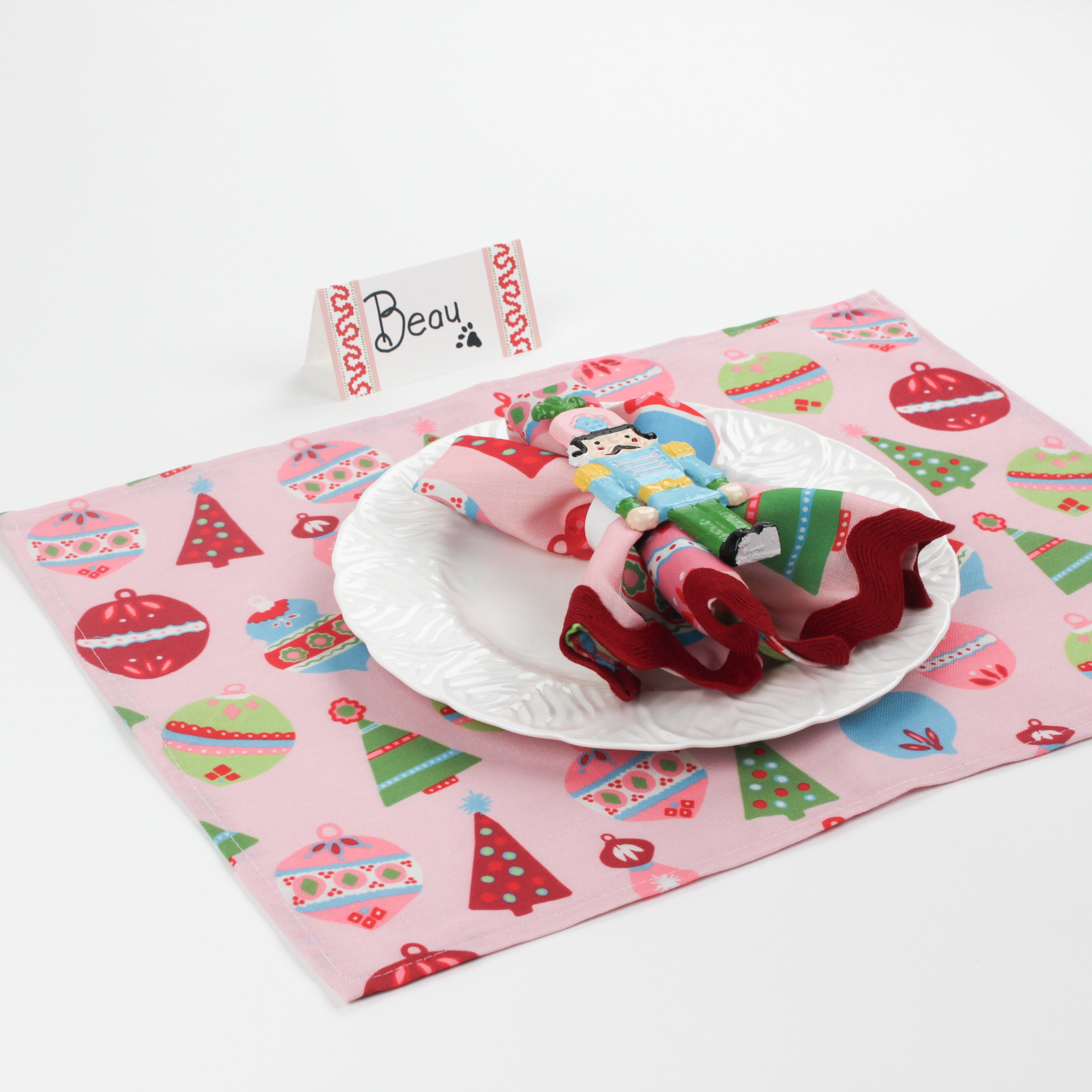 Side angle view of Harbor Trail Paper Place Card in pink and red on a Christmas-themed table with nutcracker napkin and festive pink placemat.