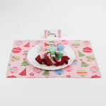 Christmas table setup featuring Harbor Trail Paper Place Card in pink and red, white plate, nutcracker napkin ring, and festive pink placemat with ornaments and trees.