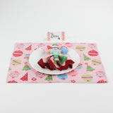 Christmas table setup featuring Harbor Trail Paper Place Card in pink and red, white plate, nutcracker napkin ring, and festive pink placemat with ornaments and trees.