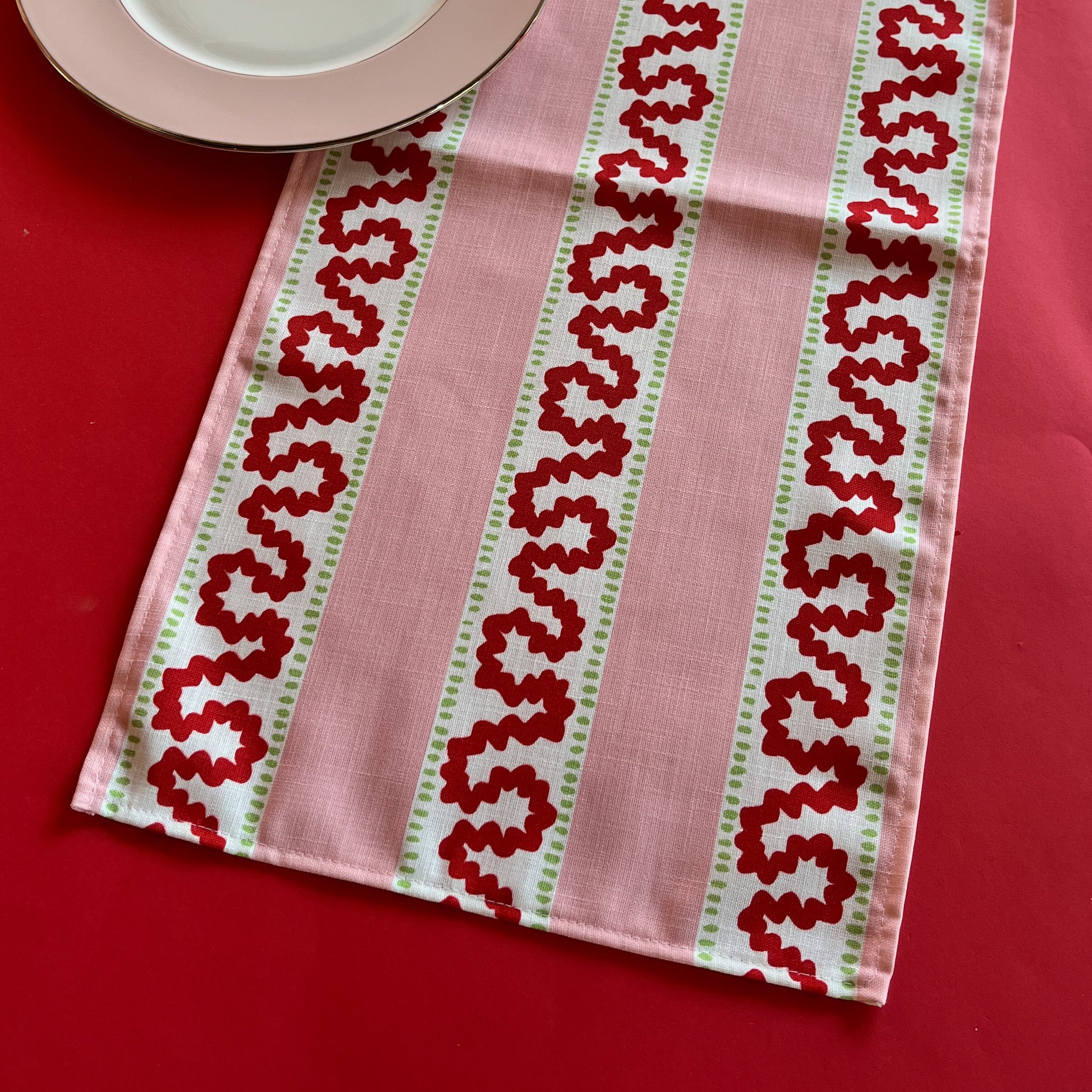 Detailed view of the Harbor Trail Pink and Red cloth table runner on a red background