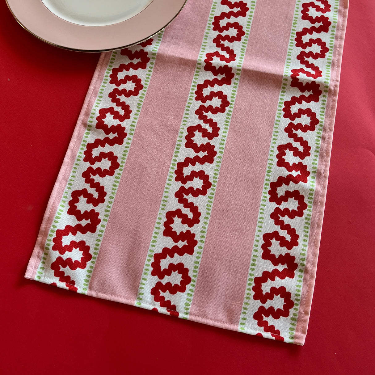 Detailed view of the Harbor Trail Pink and Red cloth table runner on a red background
