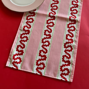 Detailed view of the Harbor Trail Pink and Red cloth table runner on a red background
