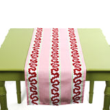 Pink and red patterned table runner displayed on a green table.