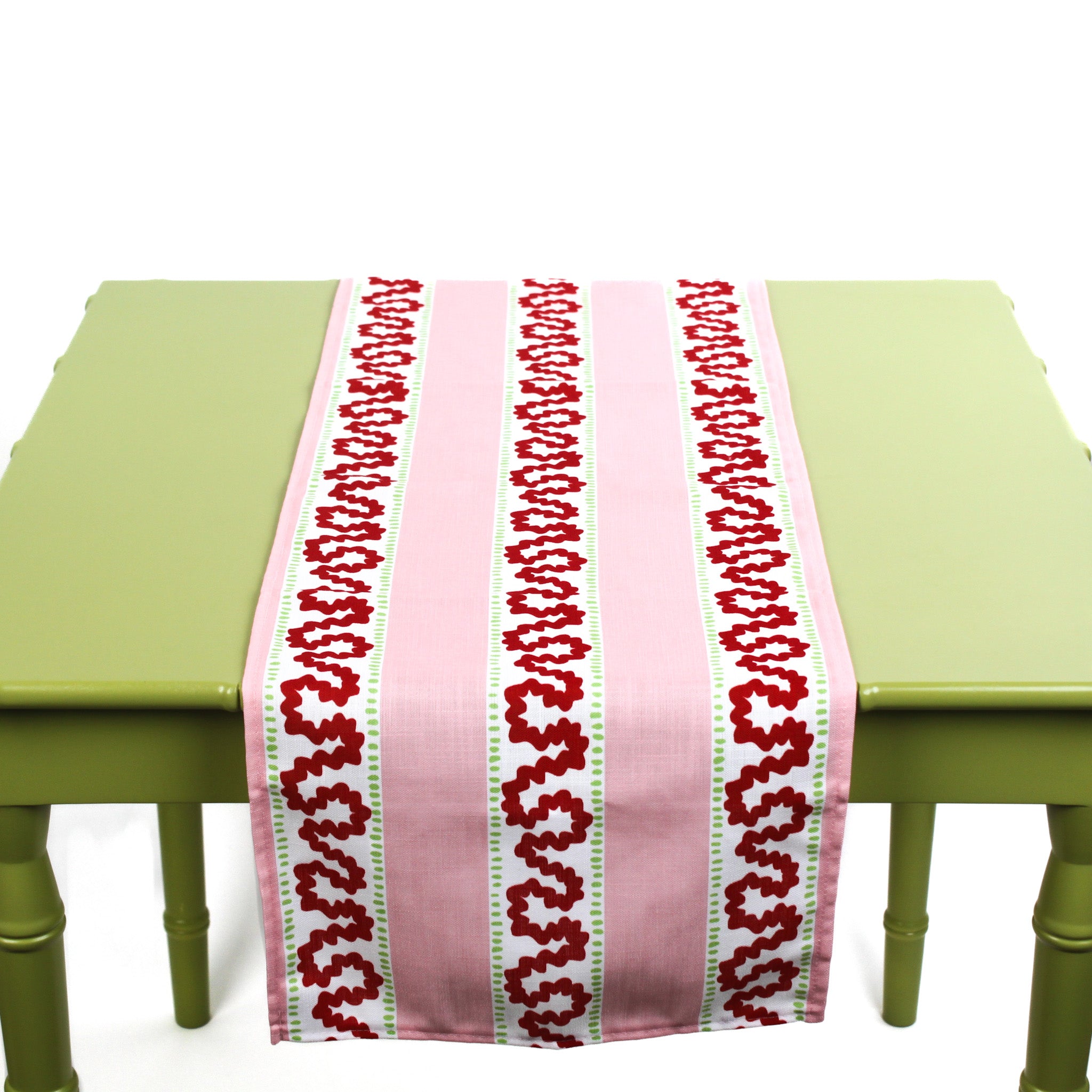 Pink and red patterned table runner displayed on a green table.