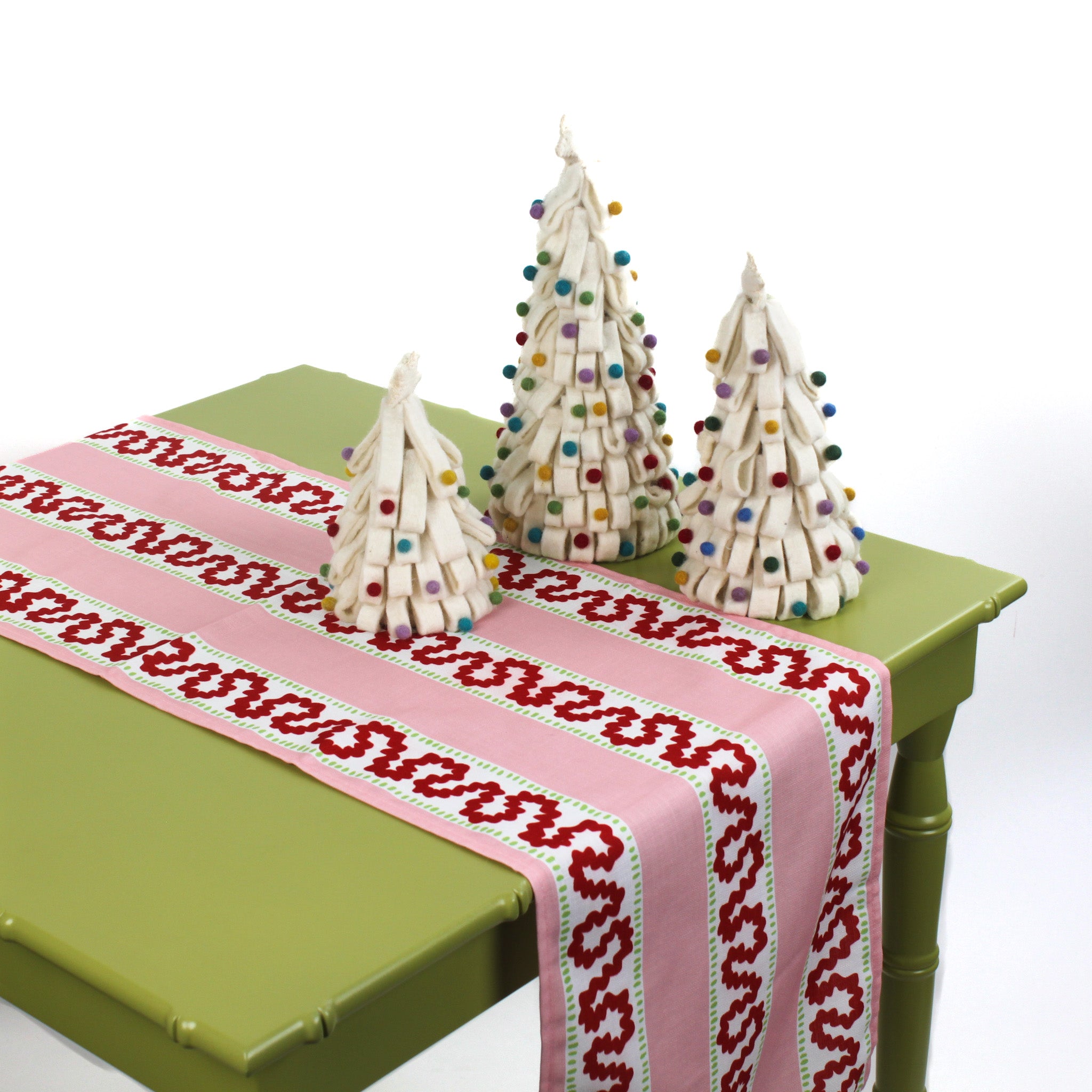 Pink and red patterned table runner on a green table with decorative Christmas trees