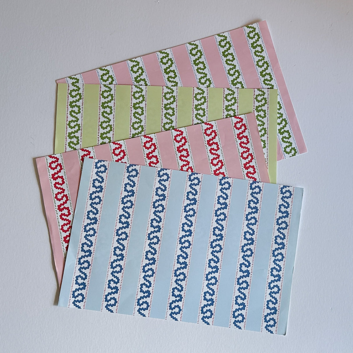 A set of rectangular paper placemats with a harbor trail pattern in alternating colors of blue, red, pink, and green.