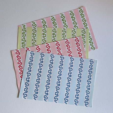 A set of rectangular paper placemats with a harbor trail pattern in alternating colors of blue, red, pink, and green.