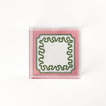 a square acrylic tray with a pink and green base featuring a green squiggle motif around the border.