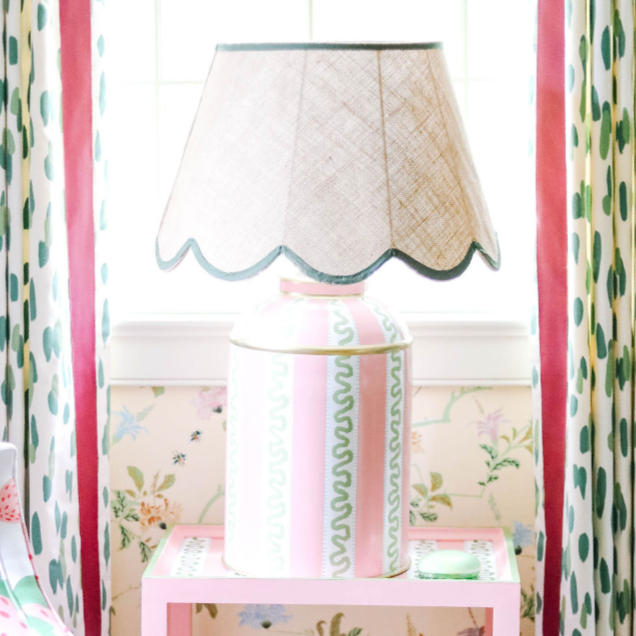 a striped white, pink and green lamp with a scalloped rattan shade with green trim sitting on a pink side table. 