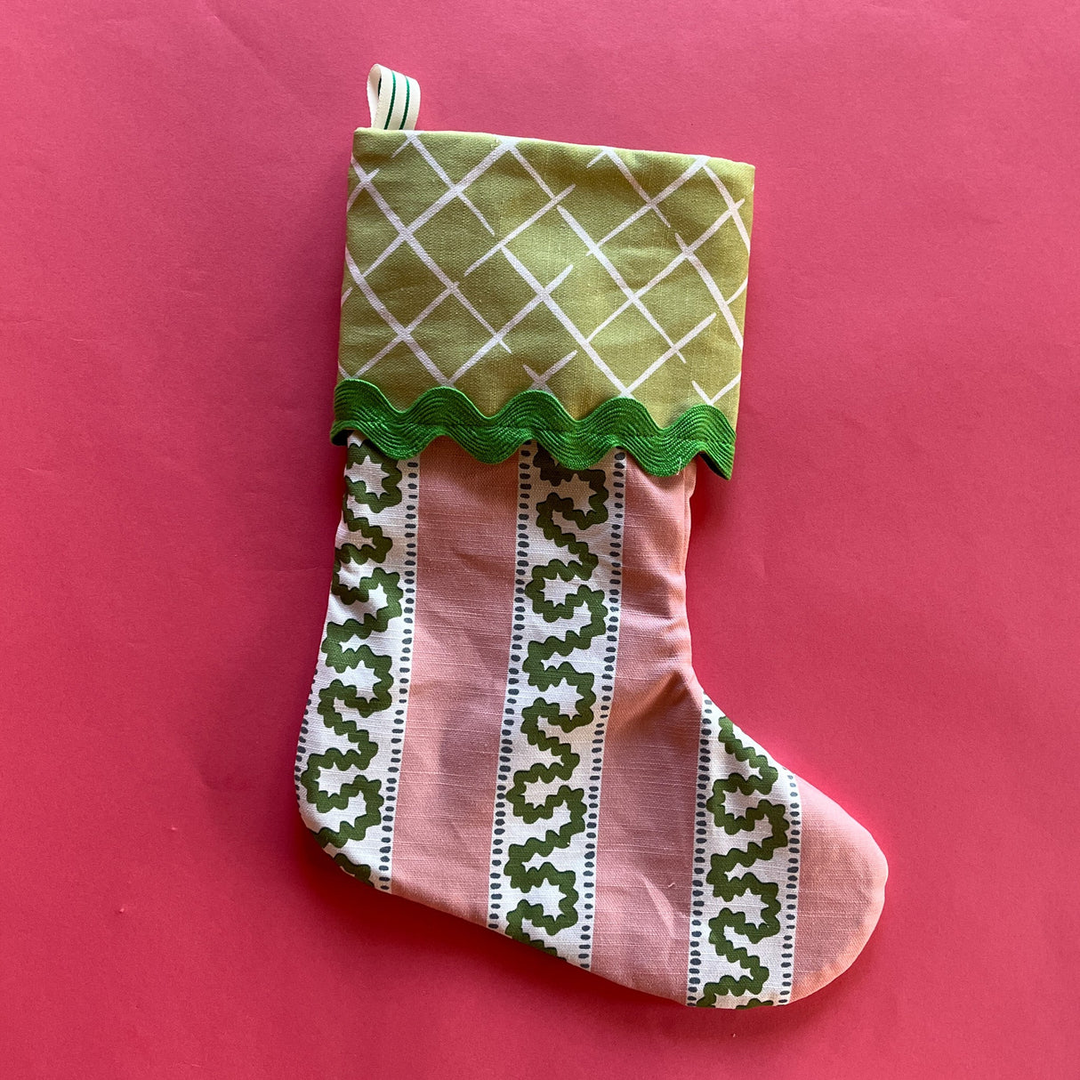 A pink Christmas stocking with a pink and green striped pattern with green fabric at the top.