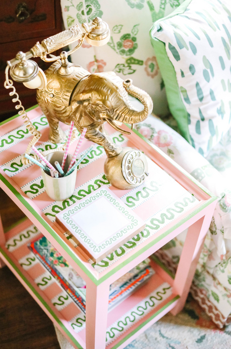 A pink side table with green and white striped accents and an elephant phone and notepad resting on top. 
