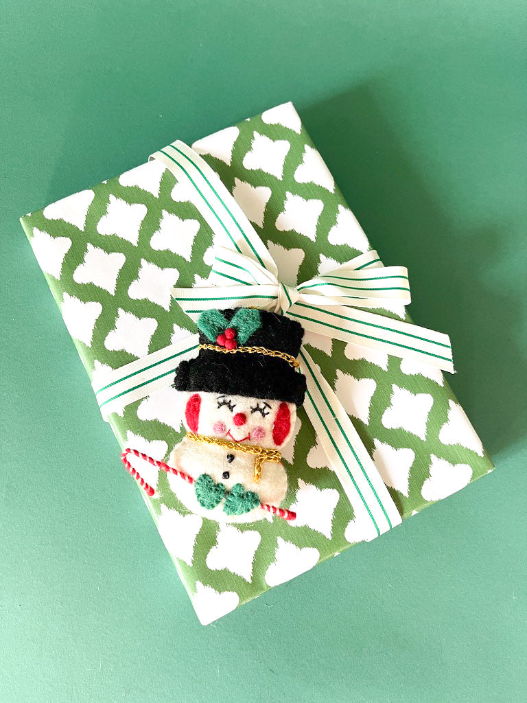Gift wrapped in green and white patterned paper with striped ribbon and felt snowman decoration.