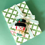 Gift wrapped in green and white patterned paper with striped ribbon and felt snowman decoration.