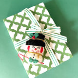 Gift wrapped in green and white patterned paper with striped ribbon and felt snowman decoration.