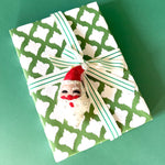 Gift wrapped in green and white patterned paper with striped ribbon and felt Santa decoration.
