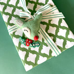 Gift wrapped in green and white patterned paper with striped ribbon and felt reindeer decoration.