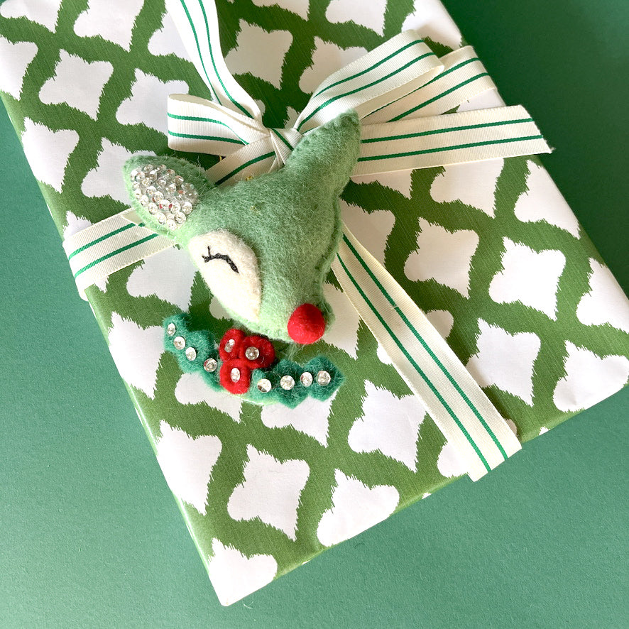 Gift wrapped in green and white patterned paper with striped ribbon and felt reindeer decoration.