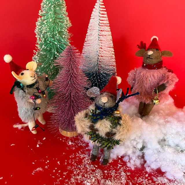 Three felt mice ornaments carrying christmas decorations around three small christmas trees on a red, snowy background