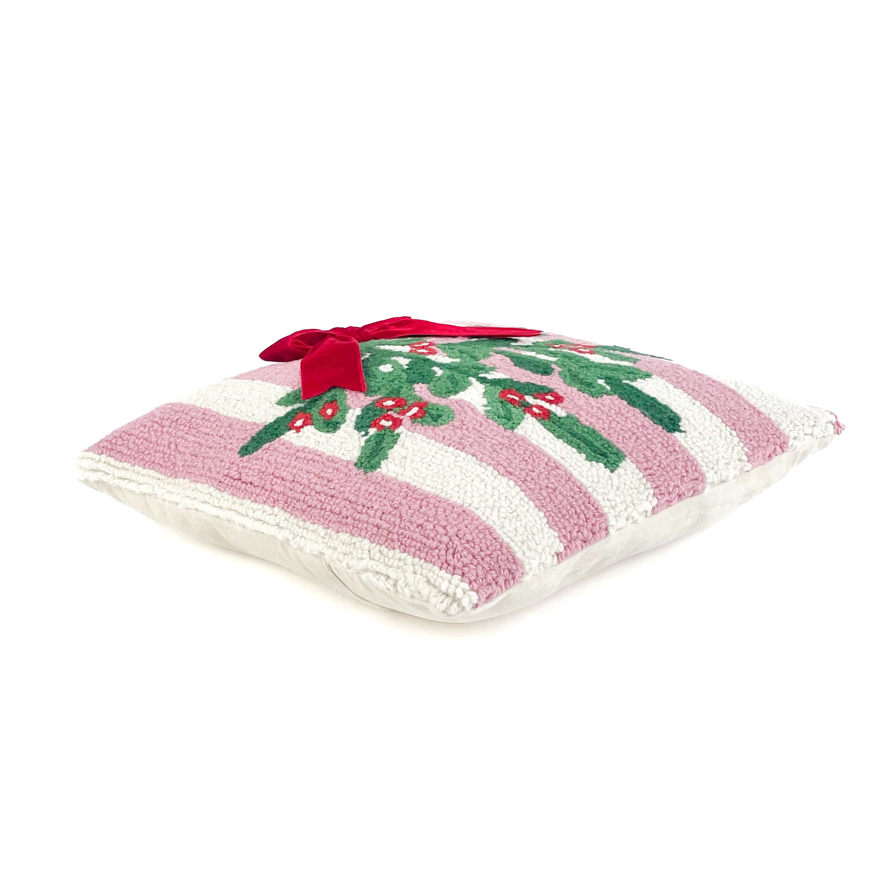 White and pink striped christmas pillow with holly design and red bow on its side on a white background.