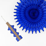 A folded blue honeycomb paper fan decoration with an attached wooden support strip beside an opened fan on a white background.