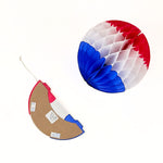A folded red white and blue honeycomb paper ball decoration shown beside an opened hanging decoration on a white background.