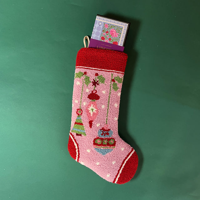 A hooked wool pink Christmas stocking featuring ornament motifs. 