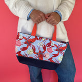 Rock Lobster small canvas tote bag with red straps and blue fabric with a repeating lobster and shell motif held by model