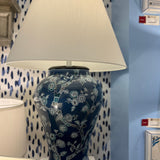 An illuminated navy table lamp featuring a blue and white chinoiserie lamp base and a white lampshade.
