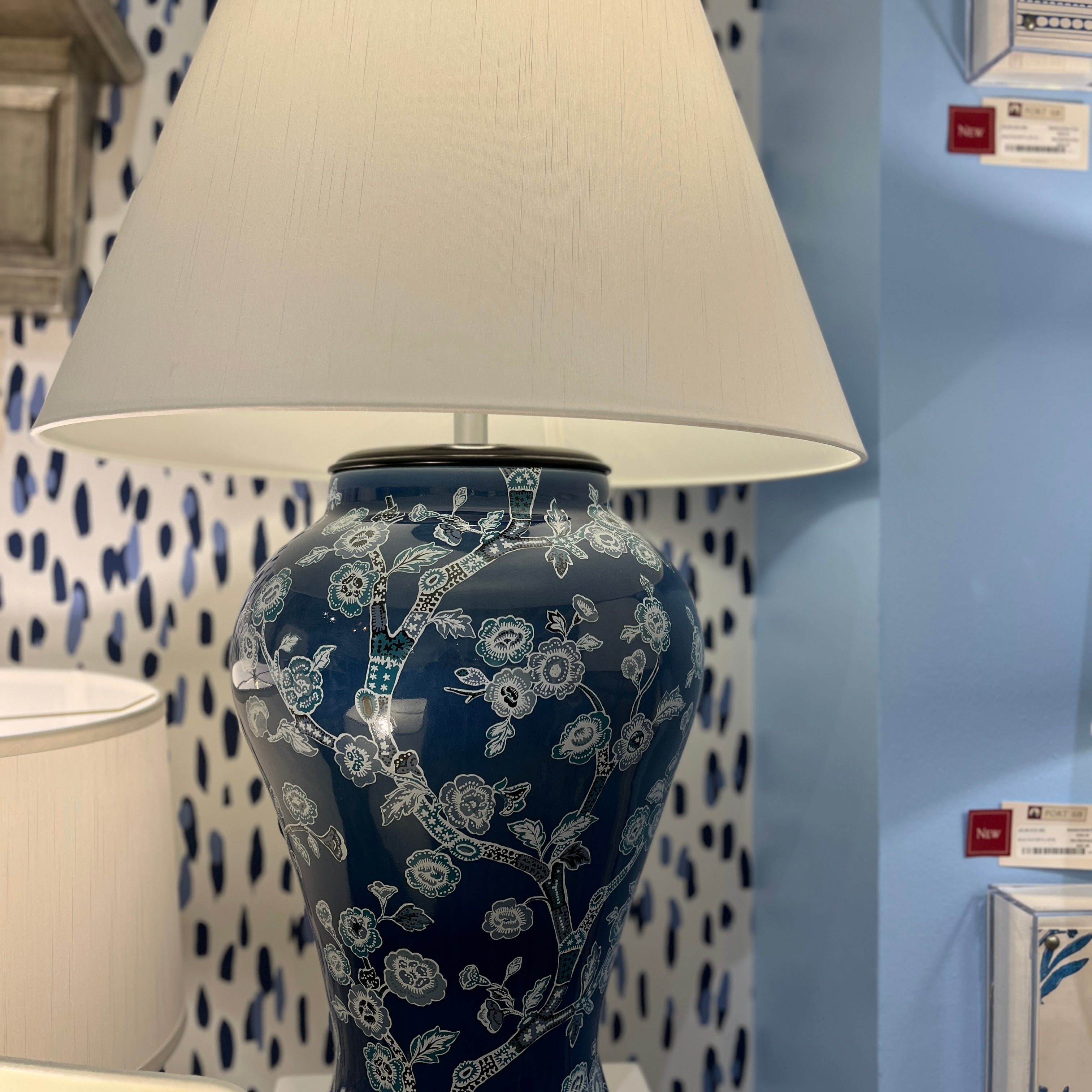 An illuminated navy table lamp featuring a blue and white chinoiserie lamp base and a white lampshade.