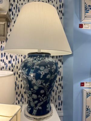 An illuminated navy table lamp featuring a blue and white chinoiserie lamp base and a white lampshade. 