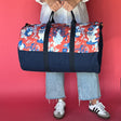 A person holding an Imperial Palace canvas duffle bag with a chinoiserie pattern on the top half and a solid navy blue color on the bottom half.