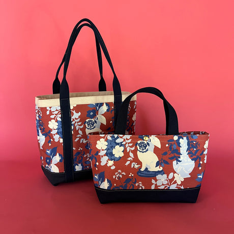 two Imperial Palace canvas tote bags, on larger than the other, in a red, white and blue chinoiserie pattern featuring white pug dogs