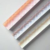 Rolls of gift wrapping paper with a geometric lattice pattern in green, blue, and pink colors.