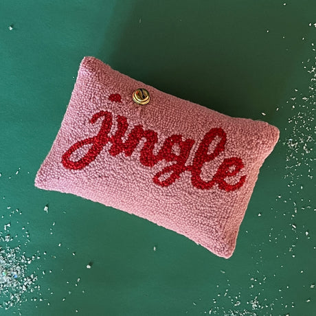 Pink Christmas Throw PIllow with red writing that says Jingle with a bell embellishment over the letter i. 