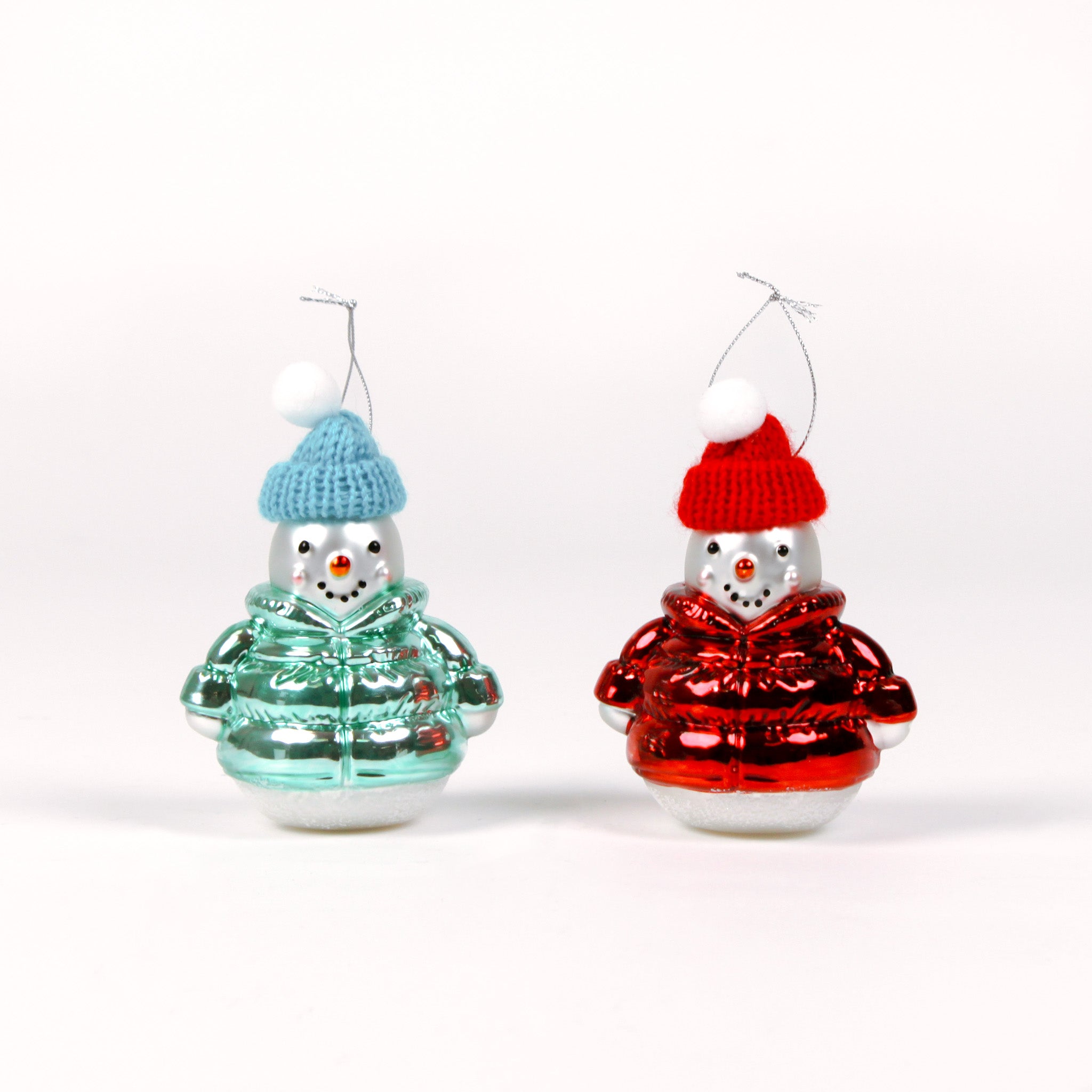 Two glass snowman ornaments, one in a green sweater and blue hat, the other in a red sweater and hat, on a white background.