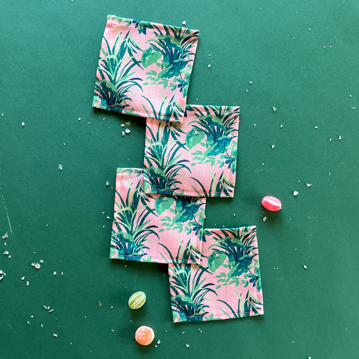 A set of bahama pink cocktail napkins in Madcap Cottages Jungle Road print, displayed on a green background with some scattered candy.
