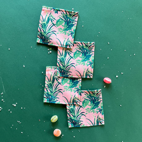 A set of bahama pink cocktail napkins in Madcap Cottages Jungle Road print, displayed on a green background with some scattered candy.