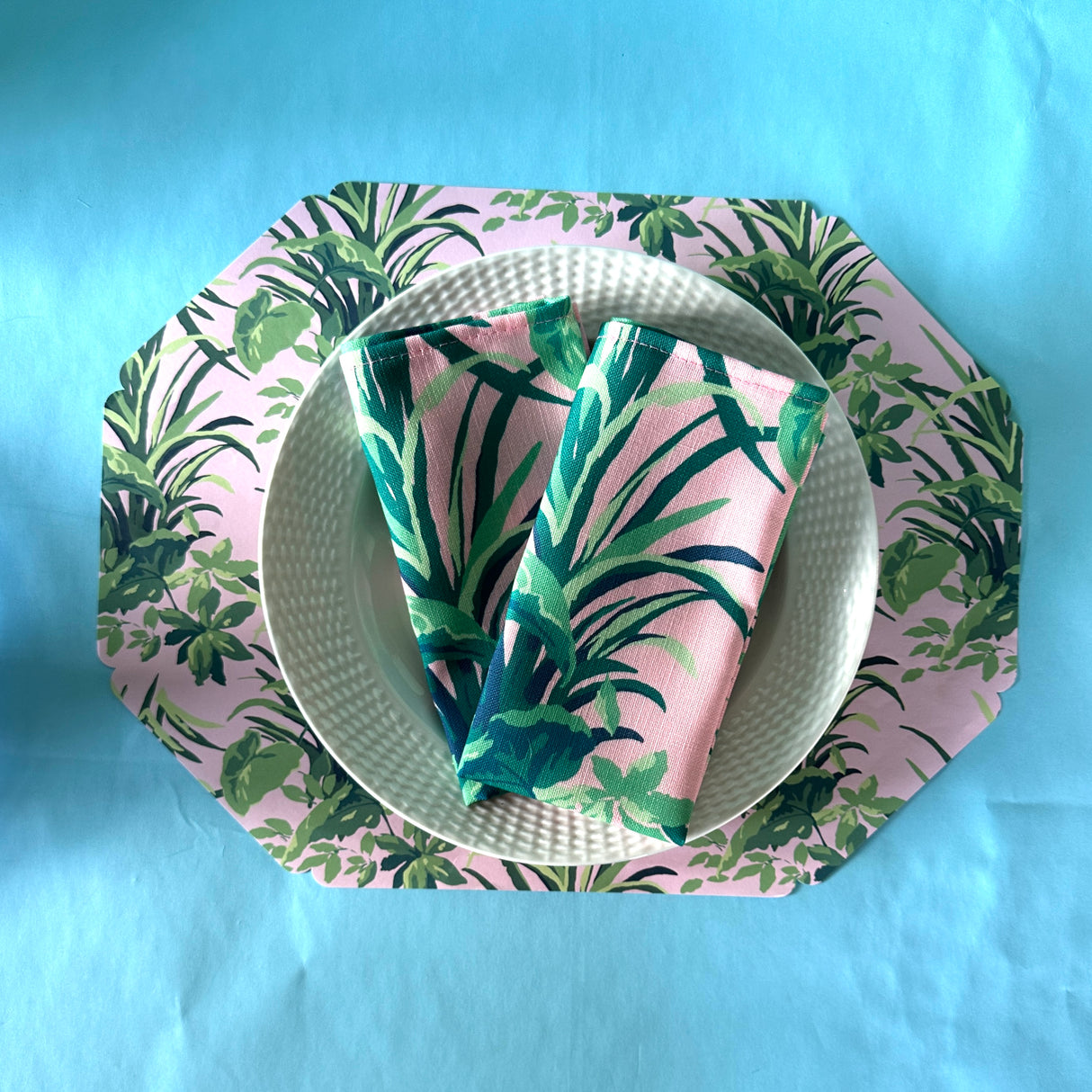 Jungle Road Bahama pinkcloth dinner napkins folded on a white plate resting on a matching placemat.