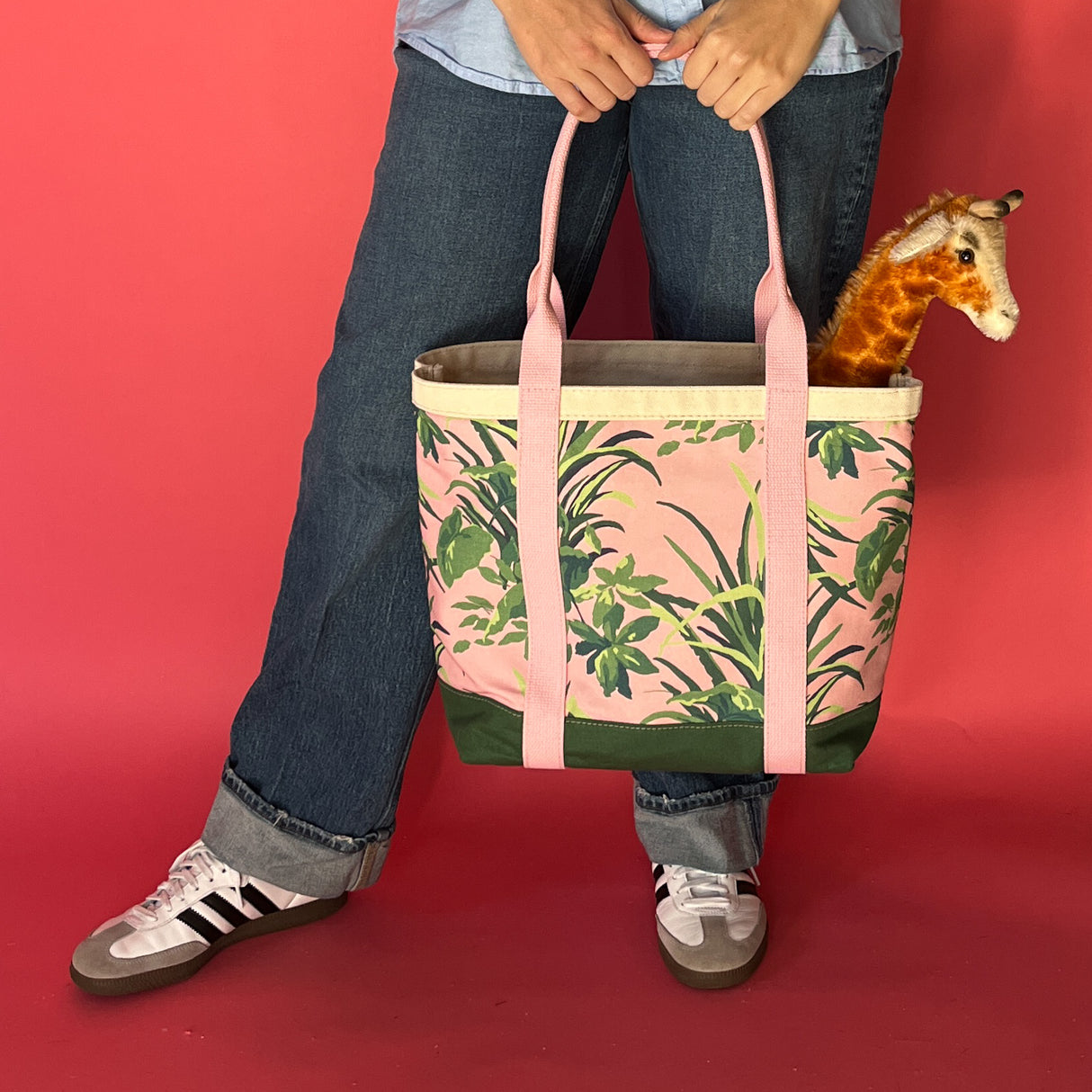 Lifestyle shot of the Jungle Road large pink and green canvas tote with a giraffe toy sticking out of the tote.