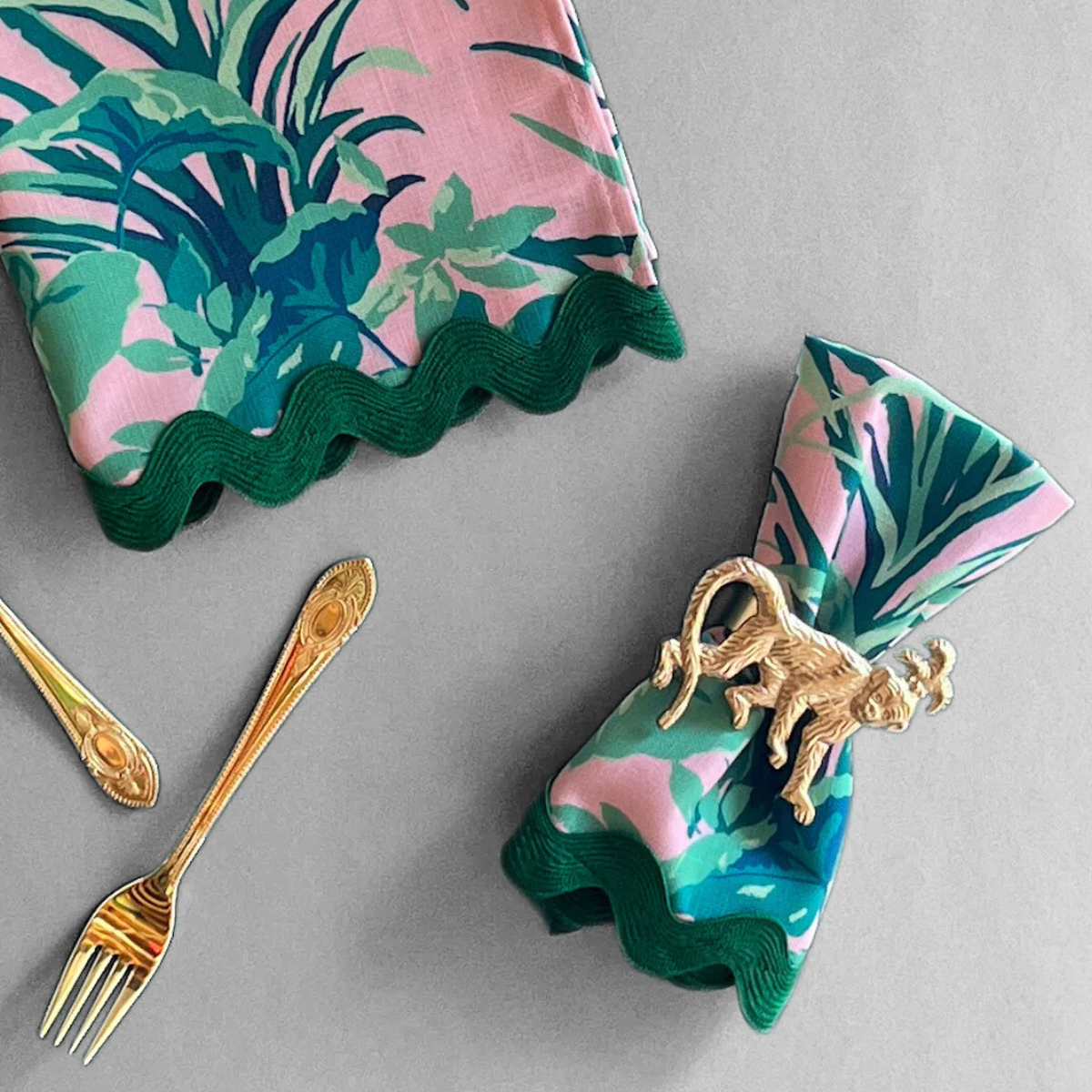 Jungle Road patterned cloth dinner napkins shown in pink with a green ric rac trim gathered with a gold monkey napkin ring.