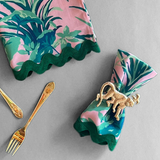 Jungle Road patterned cloth dinner napkins shown in pink with a green ric rac trim gathered with a gold monkey napkin ring.