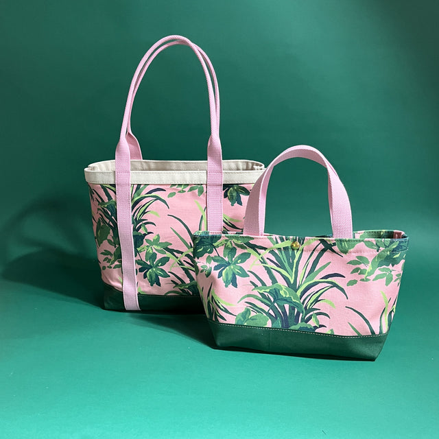 Two Jungle Road canvas tote bags with a pink and green leaf pattern, displayed against a green background.