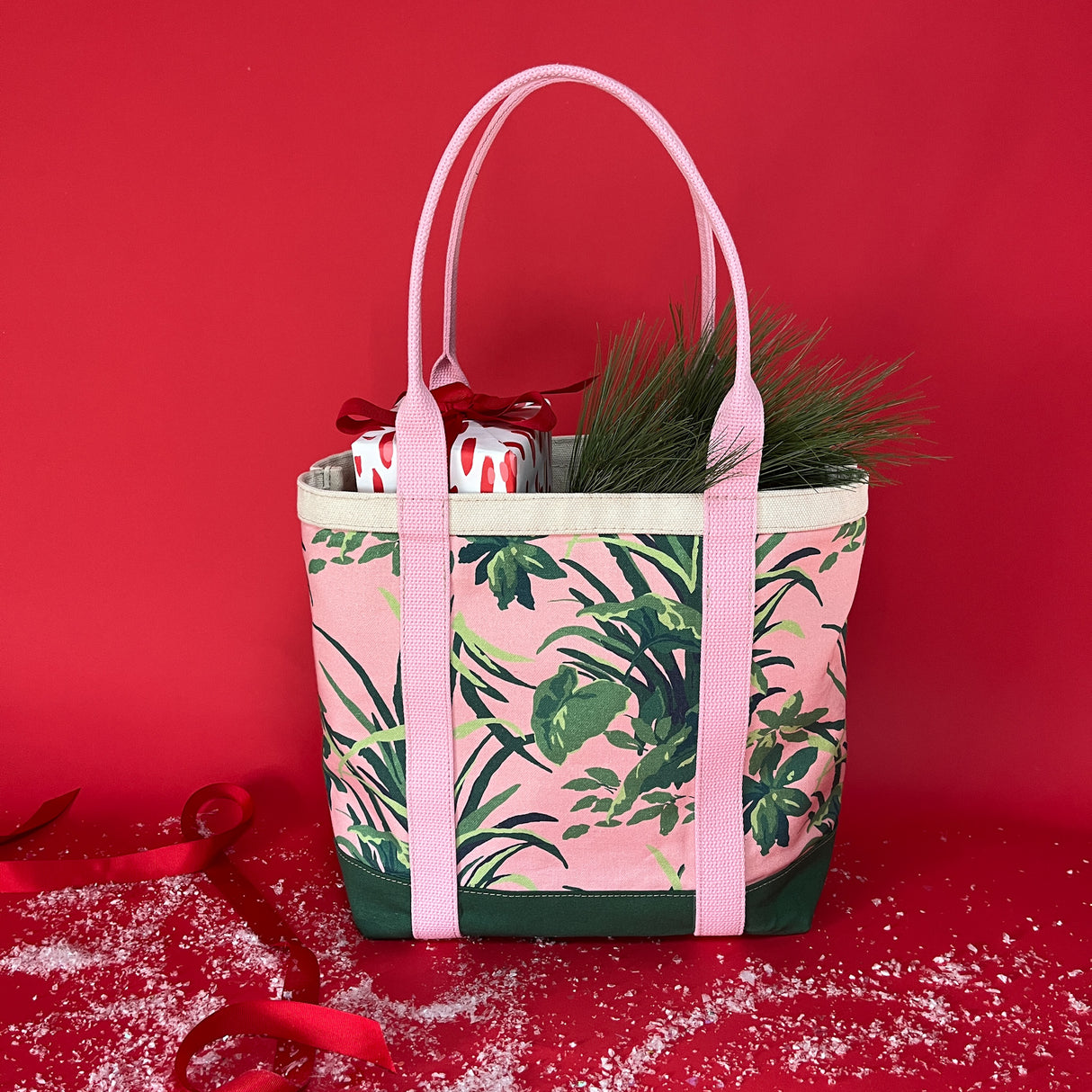 Christmas present and fir tree branch sticking out of the top of the Jungle Road large pink and green canvas tote.