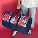Lifestyle shot of the Imperial Palace duffle bag in red and navy blue with model holding bag.