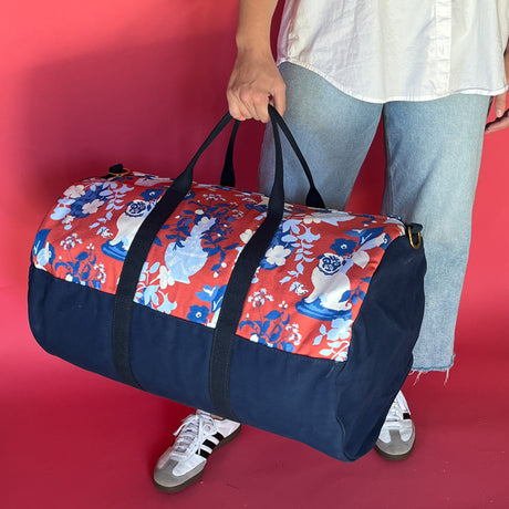 Lifestyle shot of the Imperial Palace duffle bag in red and navy blue with model holding bag.