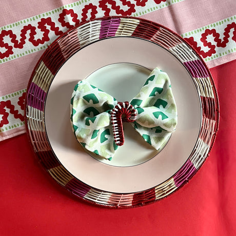 Lifestyle shot of the Peppermint rattan charger with a pink trimmed plate and napkin with candy cane rattan napkin ring
