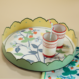 Strawberry Hill is a round tole metal tray designed by Madcap Cottage with scalloped edges and a hand painted strawberry, blue flower and lemon motifs on the base. Shown with two red and white cups with straws.