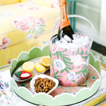 a round Temple Garden pink and green chinoiserie tole metal tray filled with small snack dishes and an acrylic ice tray filled with champagne. 