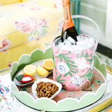 a round Temple Garden pink and green chinoiserie tole metal tray filled with small snack dishes and an acrylic ice tray filled with champagne. 